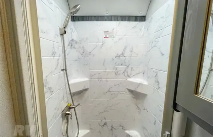 Modern RV rental shower with faux marble tile walls, a handheld showerhead, and convenient built-in shelves.. Forest River Solera 2022