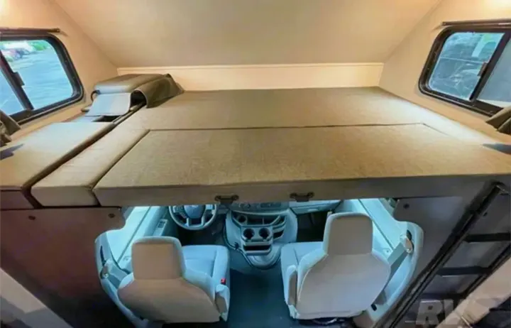 Inside an RV rental: a comfortable over-cab sleeping area viewed from above, overlooking the driver's cockpit.. Forest River Solera 2022
