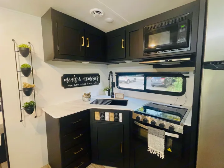 A chic, updated RV kitchen with black cabinetry, white counters, and gold hardware. Perfect for an upscale rv rental experience.. Keystone Springdale 2022