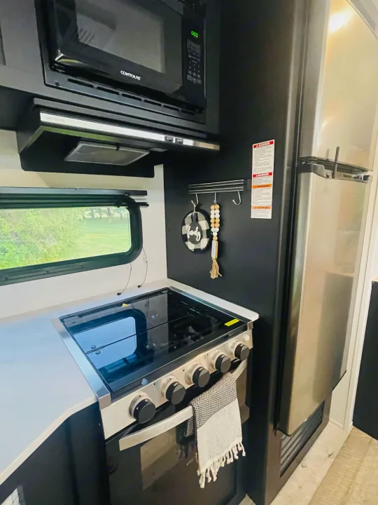 RV rental kitchen featuring a Contoure microwave, Greystone range hood, gas stove/oven, stainless fridge, and scenic window.. Keystone Springdale 2022