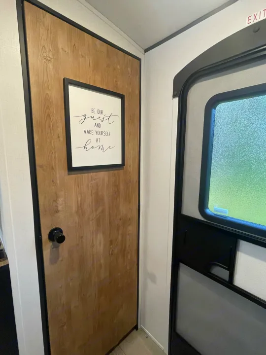 RV rental interior: Wooden door with a welcoming sign ("Be Our Guest") and main entry door with a frosted window.. Keystone Springdale 2022