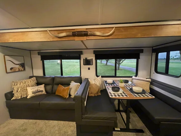 Inside a stylish RV rental: A comfy sofa, dining area with buffalo plaid, and decorative longhorn horns overhead.. Keystone Springdale 2022