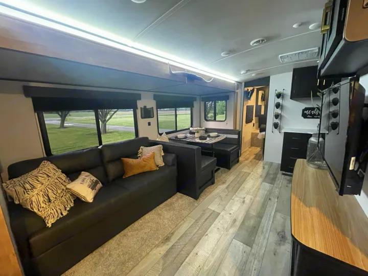 Modern RV rental interior featuring a dark sofa, dining booth, and kitchen area. Spacious layout with light flooring for comfortable travel.. Keystone Springdale 2022