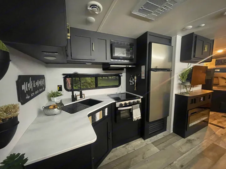 Compact, modern RV rental kitchen. Features black cabinets, white countertops, full-size fridge, stove, and microwave for travel.. Keystone Springdale 2022