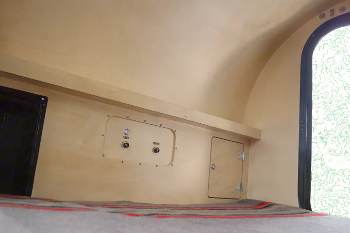 RV rental's plywood interior shows light/fan controls, storage, and a cozy sleeping area with a blanket.. Oregon Trail'R DoDrop ALPHA 2021