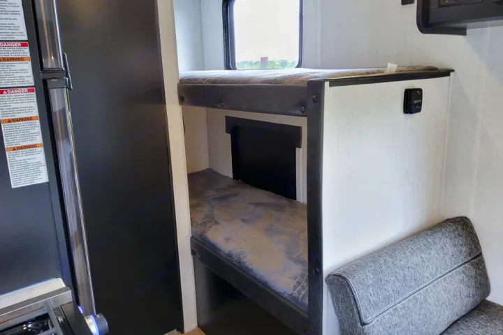 Explore this RV rental's clever interior: compact bunk beds with mattresses, a window view, and a comfy gray seating area.. Forest River Cherokee Wolf Pup 2022