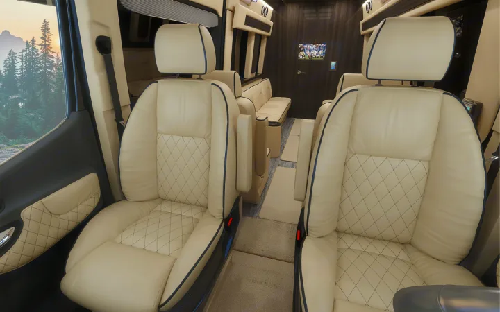 Luxurious RV rental interior with cream quilted leather captain's seats, a TV, and a scenic mountain view outside.. Ultimate Toys Ultimate Traveler 2023