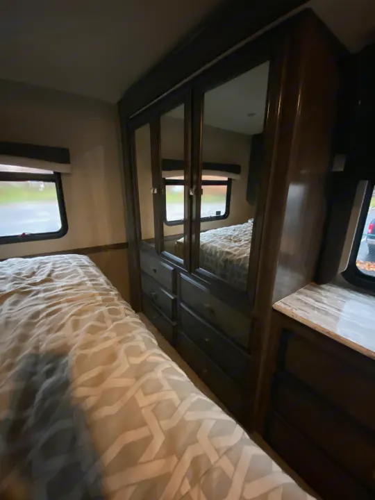 Cozy RV rental bedroom with patterned bedding, a mirrored dresser, and natural light from side windows. Ideal for travel.. Flair-Fleetwood Flair-Fleetwood Motorhome 2020