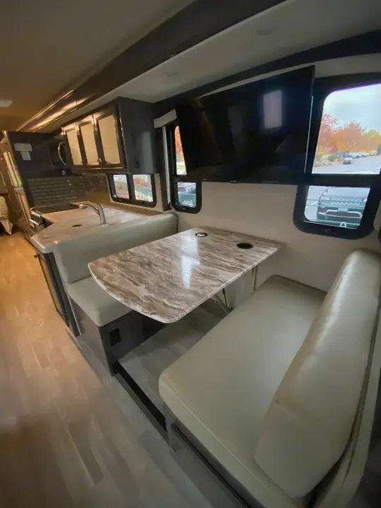 Inside this modern **rv rental**: a bright dinette with a patterned table, flat-screen TV, and functional kitchen area.. Flair-Fleetwood Flair-Fleetwood Motorhome 2020