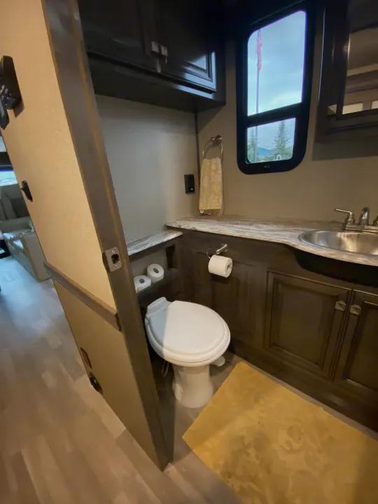 RV rental bathroom: A clean, functional space with a white toilet, sink, wood cabinets, and a window looking out.. Flair-Fleetwood Flair-Fleetwood Motorhome 2020