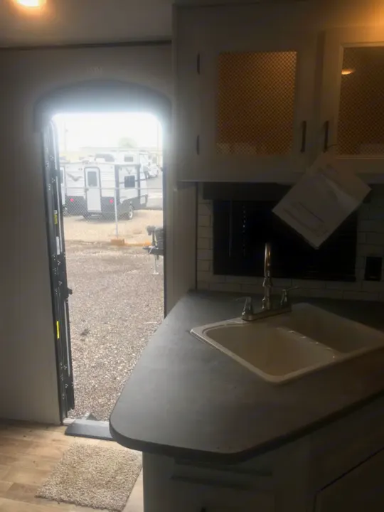 View inside an RV rental: Kitchen with sink, mesh cabinets, & open door to an outdoor lot with RVs & EXIT sign.. Keystone Hideout 2022