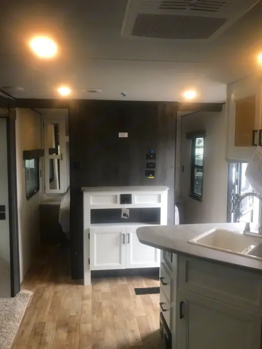 Bright RV rental interior featuring a modern kitchen, wood-look flooring, and a glimpse of the bedroom.. Keystone Hideout 2022