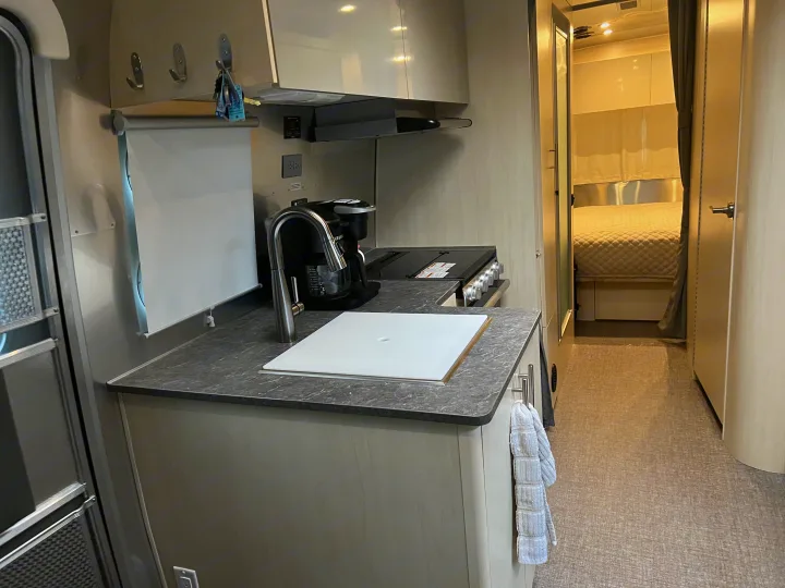 RV rental interior: A compact kitchen with sink, coffee maker, and stovetop, flowing into a cozy, well-lit bedroom.. Airstream Flying Cloud 25RB 2022