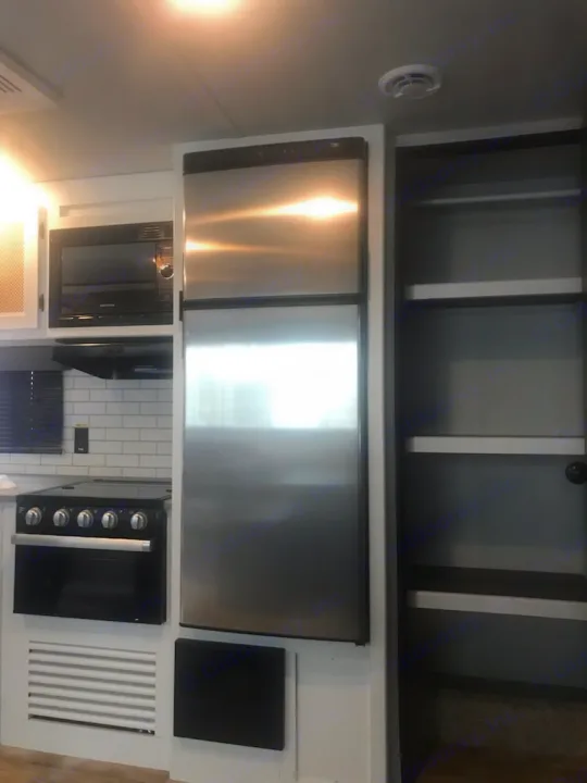 Modern RV rental kitchen featuring a stainless steel refrigerator, black microwave, and gas stove with oven.. Keystone Hideout 2022