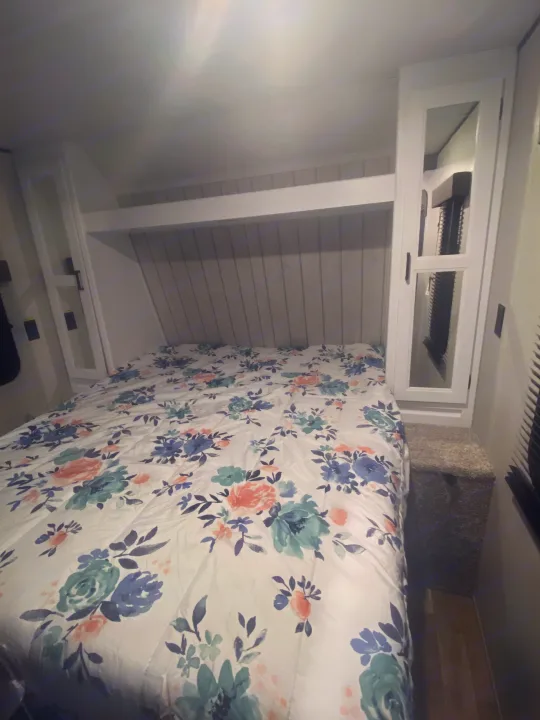 Comfortable RV rental bedroom with a bed, floral comforter, white storage, shiplap wall, and overhead AC unit.. Keystone Hideout 2022