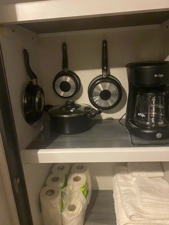 Inside an RV rental cabinet: kitchenware (pans, pot, coffee maker) above, with toilet paper and towels below.. Keystone Hideout 2022