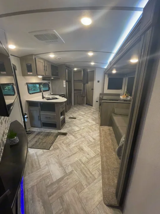 Modern RV rental interior: kitchen, living, and dining area with herringbone flooring. Bright and inviting.. Keystone RV Springdale 2021