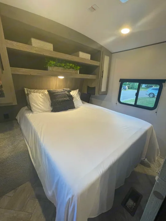 Bright RV rental bedroom: comfy bed, storage shelves, & window view. Your cozy retreat on wheels.. Keystone RV Springdale 2021