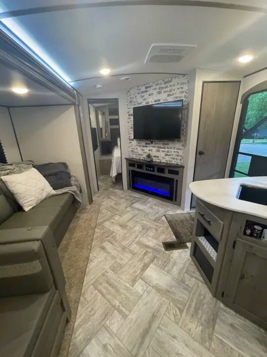 Inviting rv rental interior: living area with sofa, TV, electric fireplace, kitchen counter, and bedroom access.. Keystone RV Springdale 2021