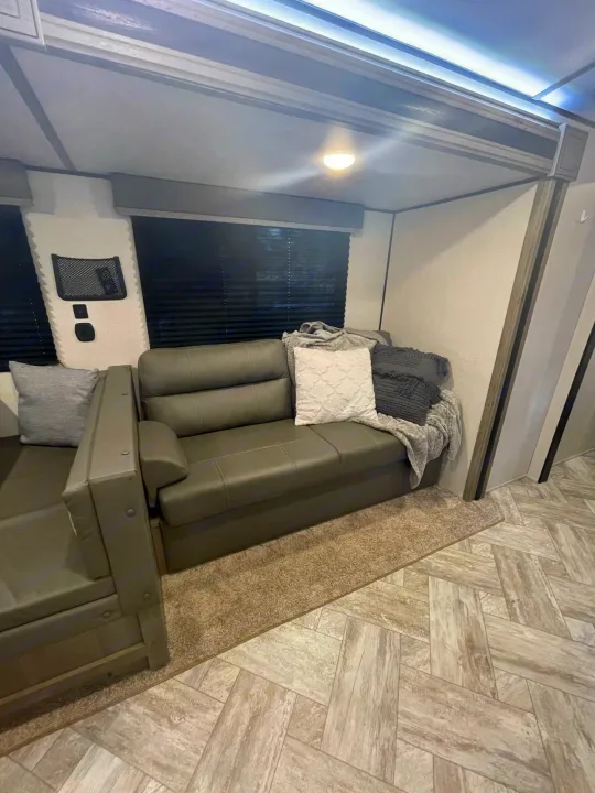 Inside this RV rental: a cozy gray sofa with plush throws, set on stylish herringbone wood-look flooring for comfort.. Keystone RV Springdale 2021