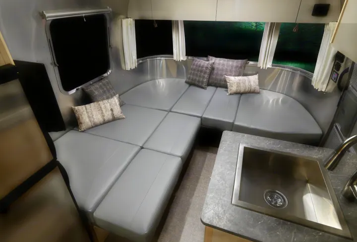 A cozy Airstream RV rental interior, showcasing flexible gray seating that converts to a bed, a kitchen sink, and windows.. Airstream Flying Cloud 25RB 2022