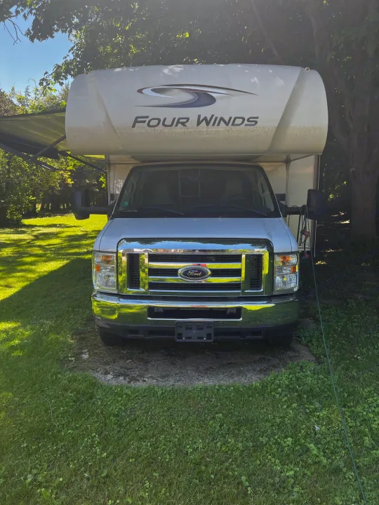 Front view of a white Ford Four Winds Class C RV rental. Parked in a sunny, grassy area with trees, ready for your next adventure.. Thor Motor Coach Four Winds 2019