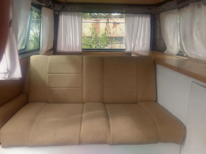 Cozy tan bench seating and windows with white curtains inside an RV rental, offering comfortable interior space for travel.. Volkswagen Westfalia 1986