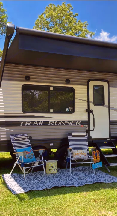 Sunny RV rental scene: a "Trail Runner" travel trailer with its awning extended over cozy outdoor chairs & rug.. Heartland RVs Trailrunner 2021