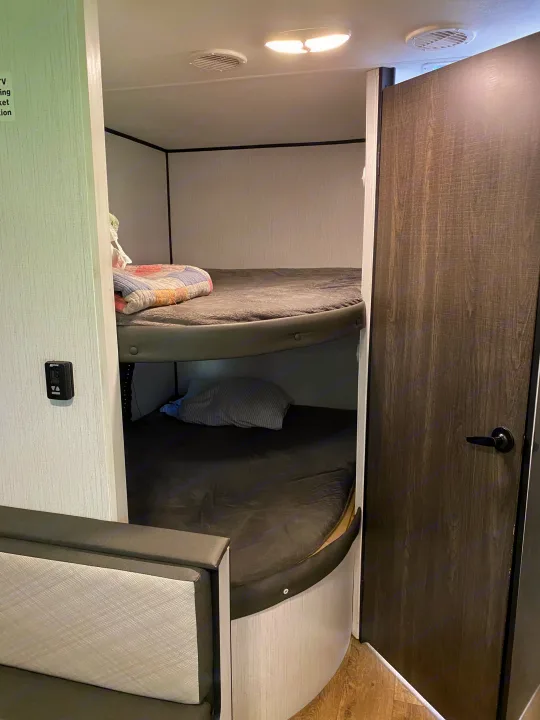 RV rental bunk beds: a cozy sleeping space with two levels, blankets, pillows, and functional interior elements.. Heartland RVs Trailrunner 2021