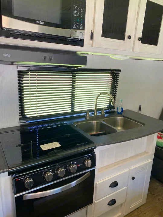 Inside this RV rental, find a bright, compact kitchen with High Pointe microwave, Suburban range, and double sink.. Heartland RVs Trailrunner 2021