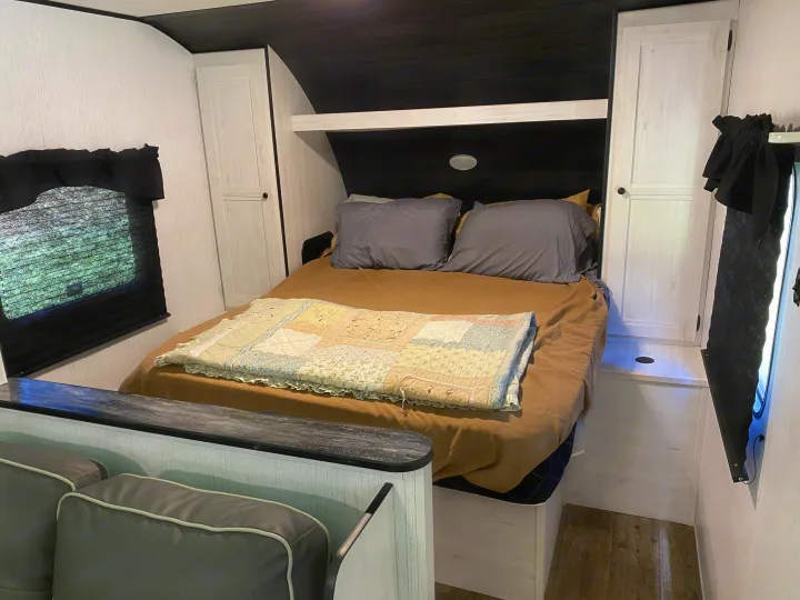 Cozy RV rental bedroom featuring a large bed with grey pillows, white cabinets, and dark wood ceiling. Ideal for travel.. Heartland RVs Trailrunner 2021