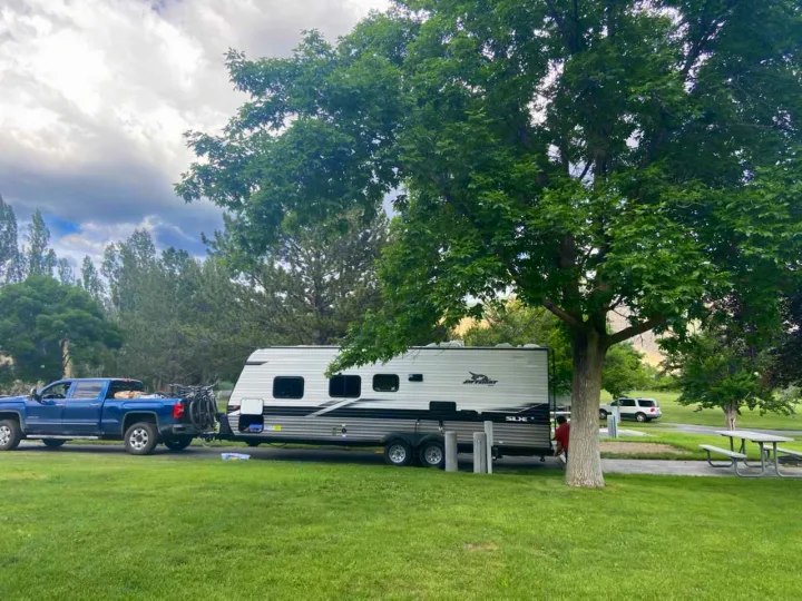 An RV rental, towed by a blue truck, is set up at a scenic campsite with a picnic table and large tree.. Jayco Jayco Jay Flight SLX 264bhw 2022