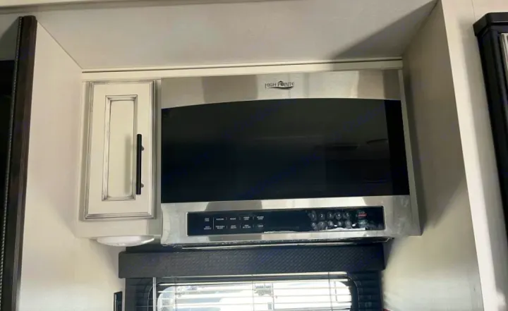 Stainless steel High Pointe microwave and white cabinet in an RV rental kitchen interior, with blinds below.. Jayco Eagle HT 2020