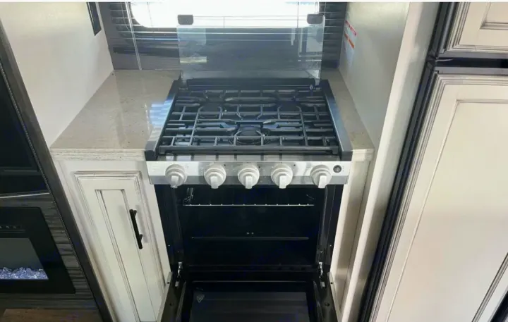 Compact gas range/oven with open door inside an RV rental, featuring stovetop, light countertops & white cabinets.. Jayco Eagle HT 2020