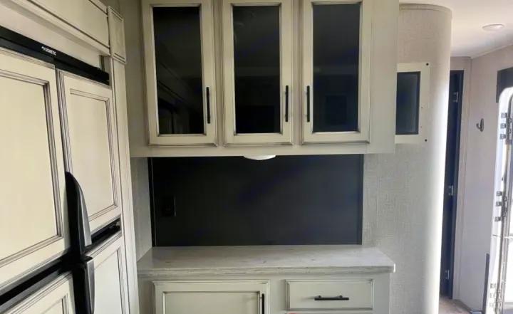 Explore this RV rental's modern interior: cream kitchen with glass-front cabinets, dark backsplash, bright counter, and large fridge.. Jayco Eagle HT 2020
