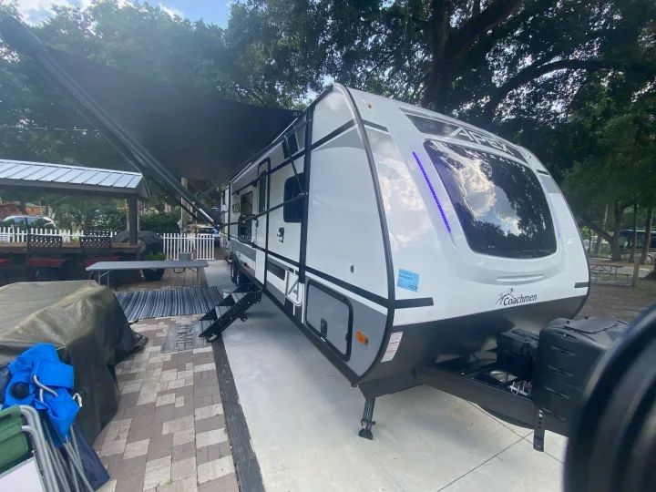 A white and grey travel trailer with extended awning, perfect for an RV rental at a scenic outdoor campsite.. Forest River two bedroom Apex ultralite 2022