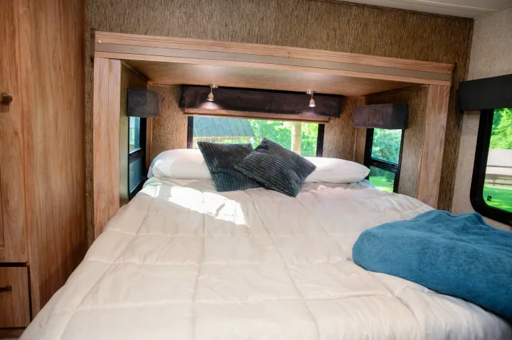 Cozy RV rental bedroom with a queen bed, white bedding, accent pillows, and windows revealing nature views.. Forest River Forester MBS 2018