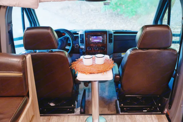 Cozy RV rental interior showing front seats, a small table with two mugs, and the cockpit view outside.. Forest River Forester MBS 2018