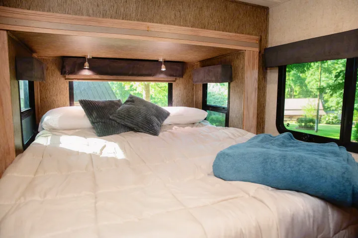 Cozy RV rental bedroom with a bright, comfortable bed, soft pillows, blue blanket, and scenic window views.. Forest River Forester MBS 2018