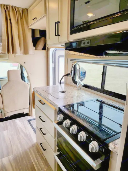 Spacious RV rental interior featuring a modern kitchen with a black stove/oven, granite-look counter, sink, microwave, and light wood flooring.. Thor Freedom Elite 2022
