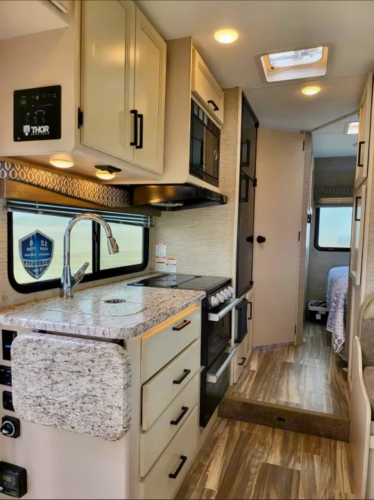 Get a feel for this RV rental's well-equipped kitchen featuring a stove, sink, and cabinets, leading to the living and bed area.. Thor Freedom Elite 2022