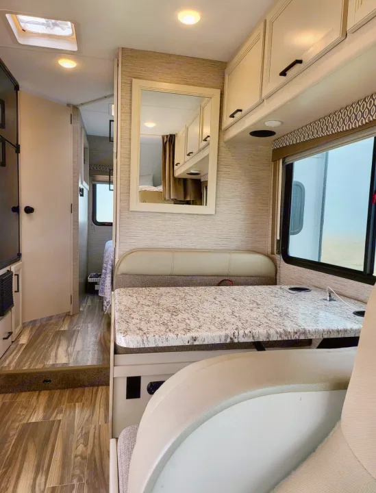Modern RV rental interior showing a dinette with a speckled countertop, overhead storage, and hallway to the bedroom.. Thor Freedom Elite 2022