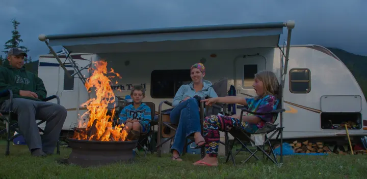 A family relaxes by a vibrant campfire in front of their RV rental. Kids and parents enjoy the evening outdoors.. Heartland RVs North Trail 2013
