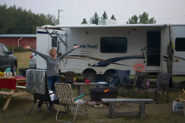 Happy woman enjoying her **RV rental** campsite with a cozy fire under an open sky.. Heartland RVs North Trail 2013