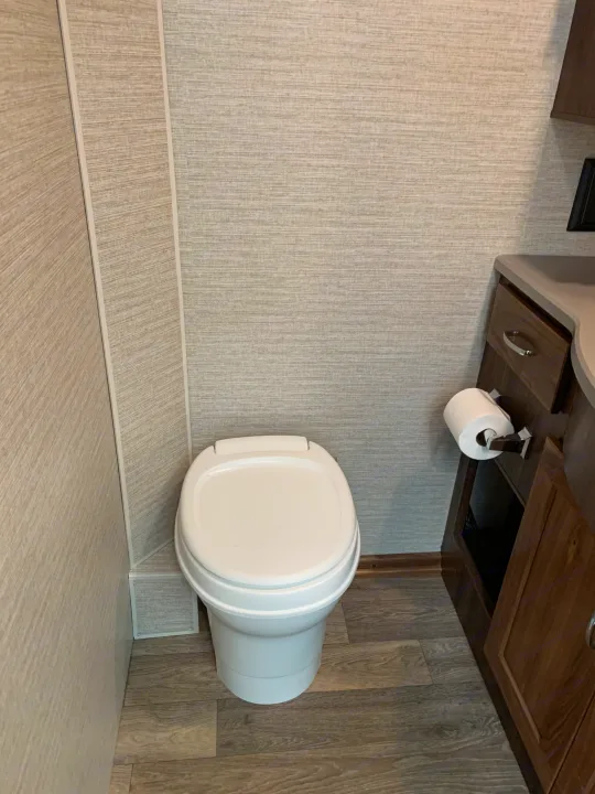 Clean RV rental bathroom features a white toilet, light textured walls, and wood-look flooring, offering comfort on your journey.. Winnebago Outlook 2020
