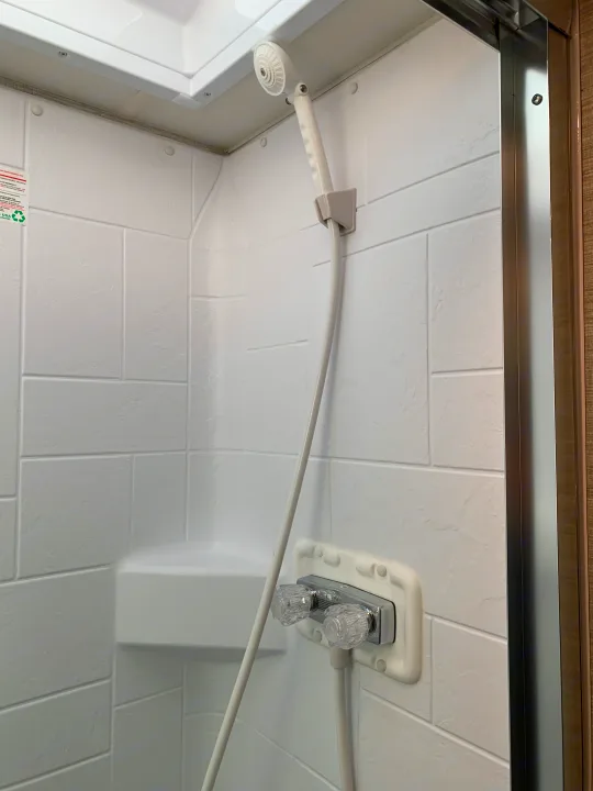 Inside an RV rental shower, featuring white faux-tiled walls, a handheld showerhead, and clear plastic hot/cold water controls.. Winnebago Outlook 2020