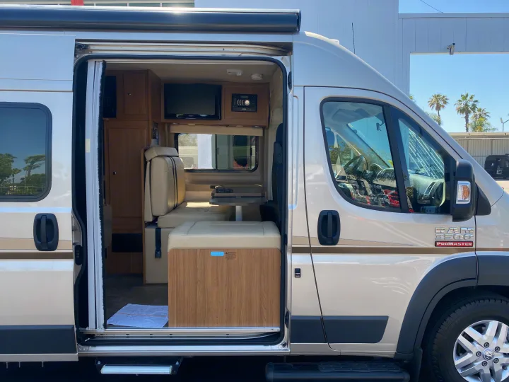 Open side of a beige Ram ProMaster camper van rv rental, showcasing its inviting interior with seating and TV.. Winnebago Travato 2014
