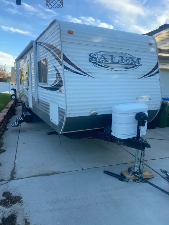 White Salem travel trailer parked on a driveway, ready for RV rental. Shows side profile, front hitch, and propane tanks.. Forest River Salem 2011