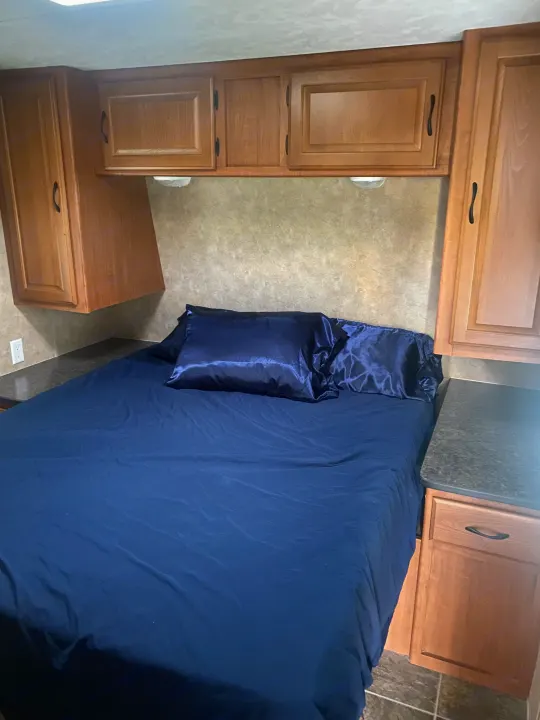 RV rental bedroom with blue bedding, satin pillows, wooden cabinets, and a nightstand, offering a compact, functional space.. Forest River Salem 2011