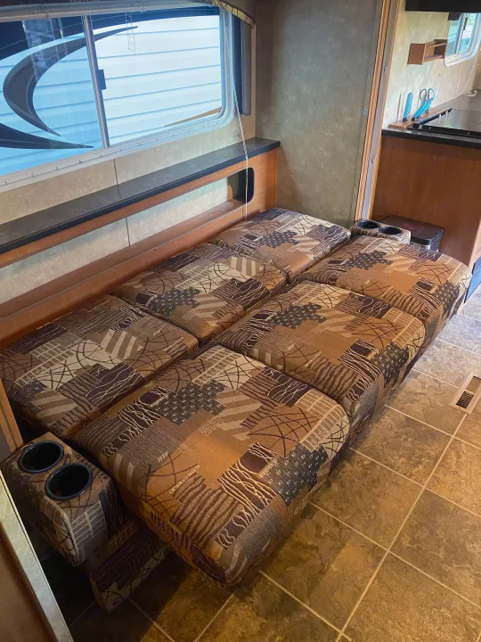 Cozy RV rental interior: patterned bench seating converts to a bed, integrated cupholders, compact kitchen, and large window.. Forest River Salem 2011
